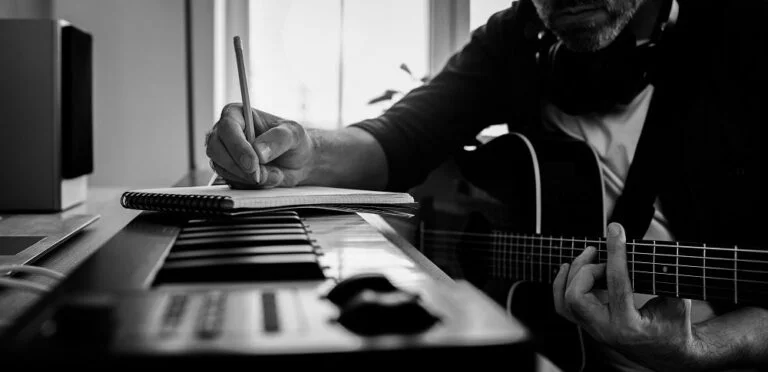 HeroImage_Man-sitting-at-keyboard-guitar-writing-on-notepad