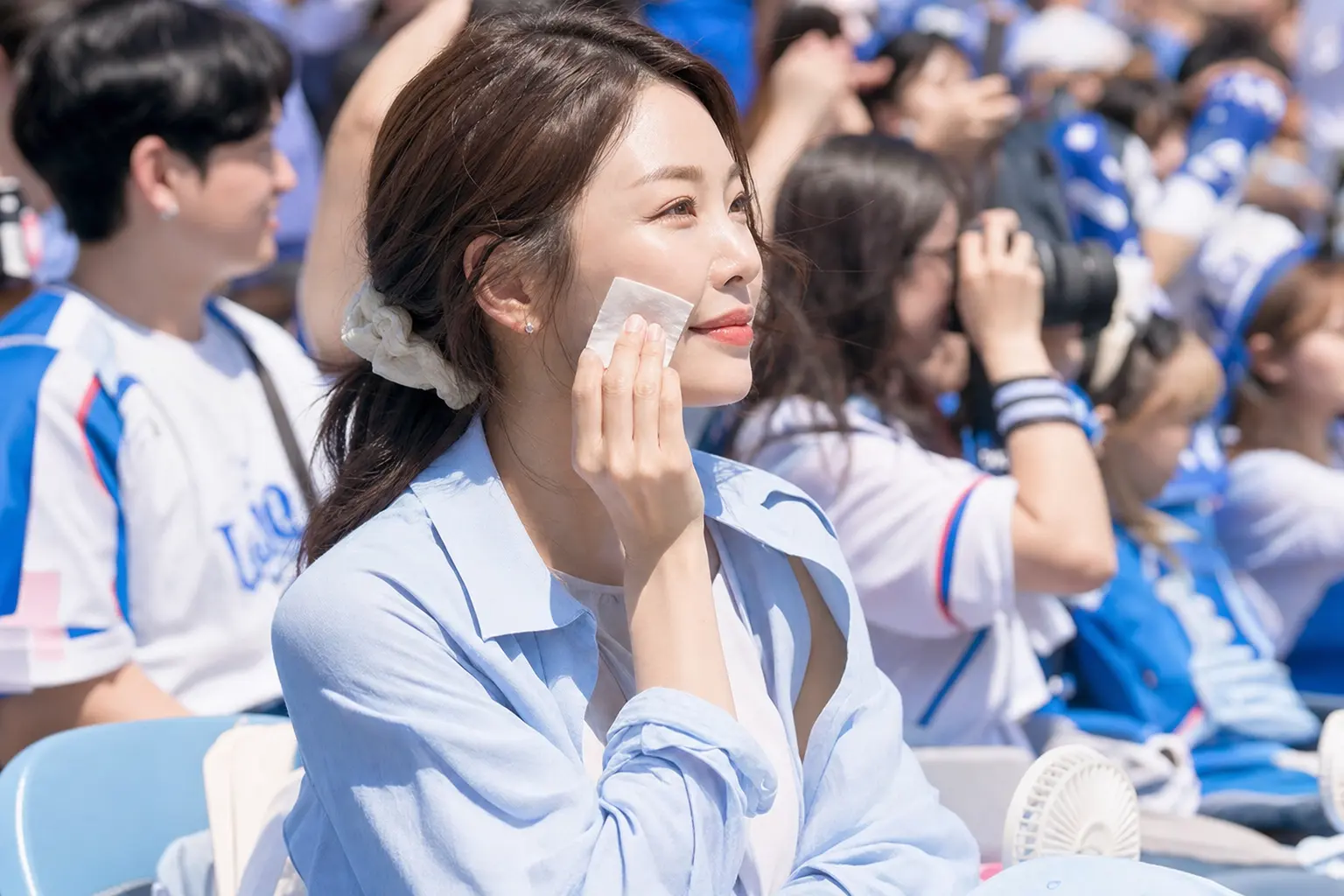 For the sweat-proof K-beauty makeup section: A candid portrait of a parent in the stands dabbing their face with blottin